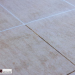 Close-up of beige ceramic tiles with white grout lines; a hairline crack runs along one grout seam near the center.